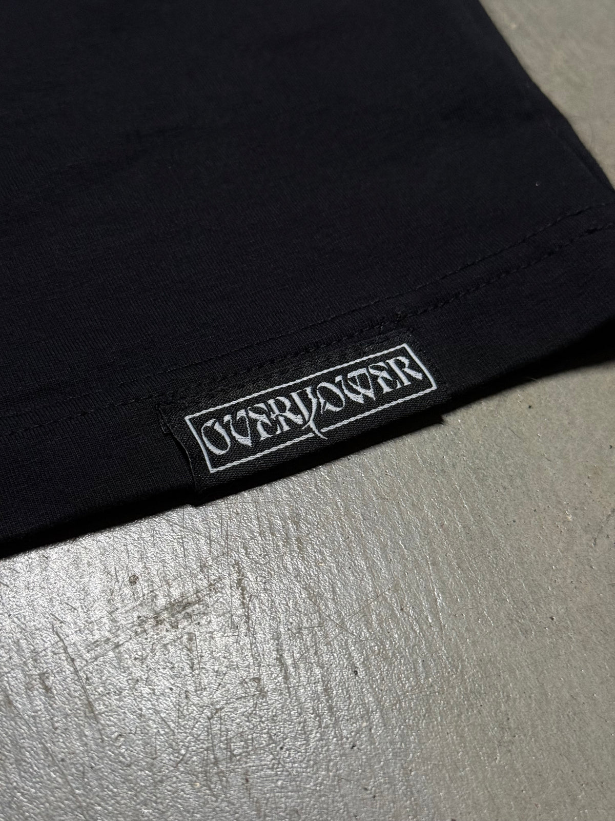 OverPower woven label sewn on the hem of the oversized tee